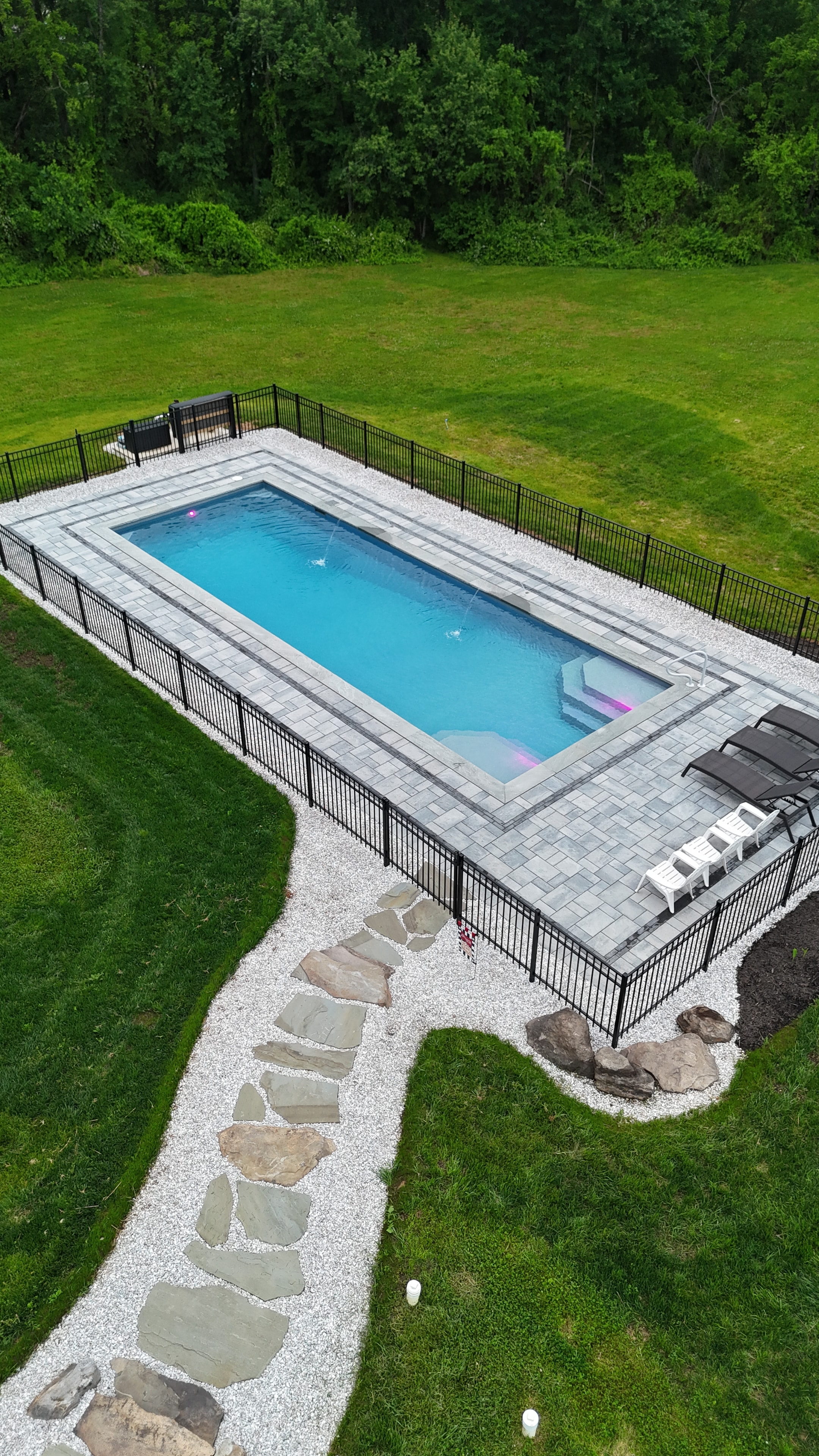 LandPro aerial daytime shot of pool with paver surround, flagstone path, white gravel, and boulder sitting wall