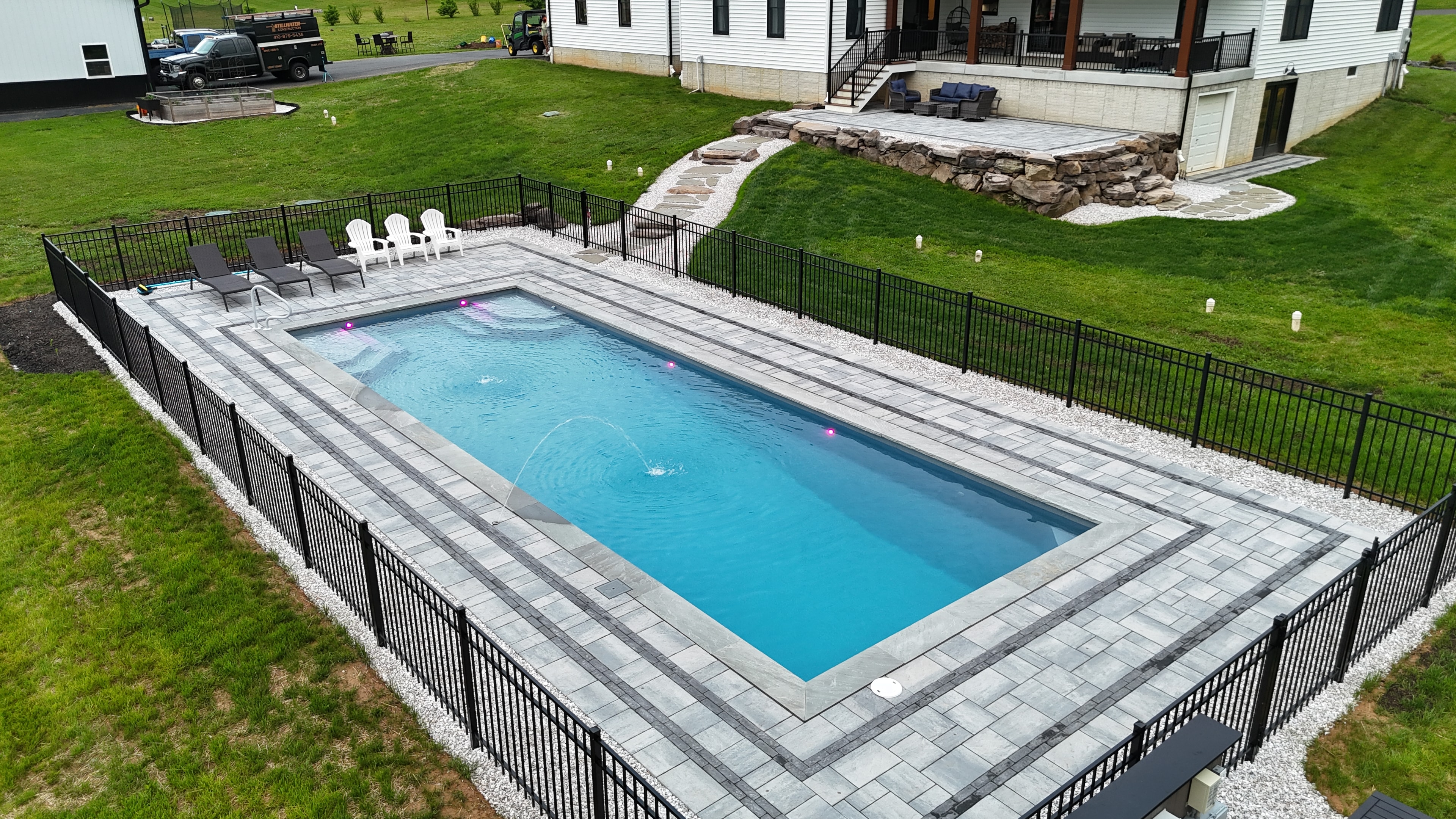 LandPro pool with paver surround, black aluminum fence, lounge chairs, and fountain jets beside new construction home
