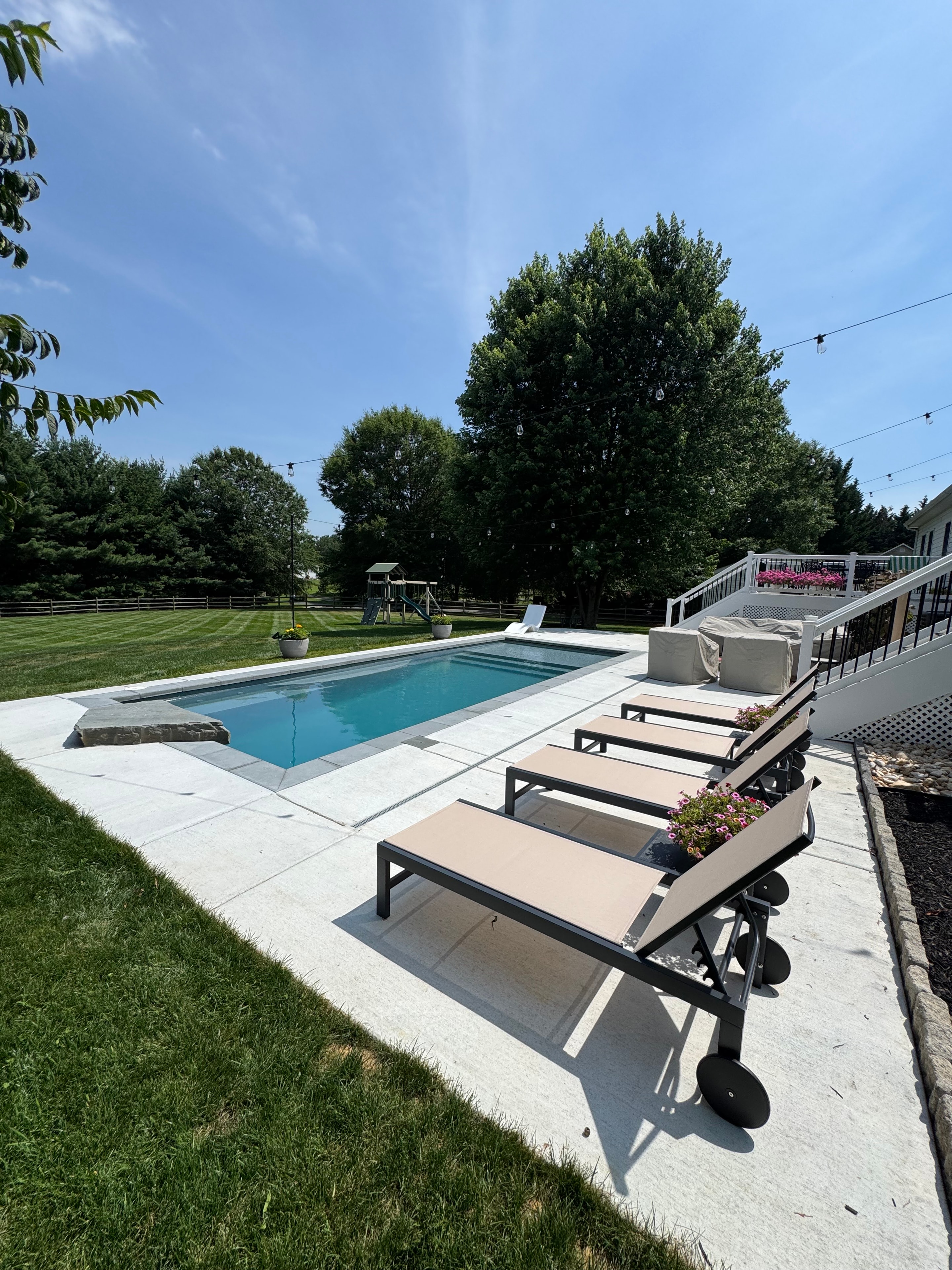 Backyard for the Kids — lounge chairs along pool edge with string lights and deck above