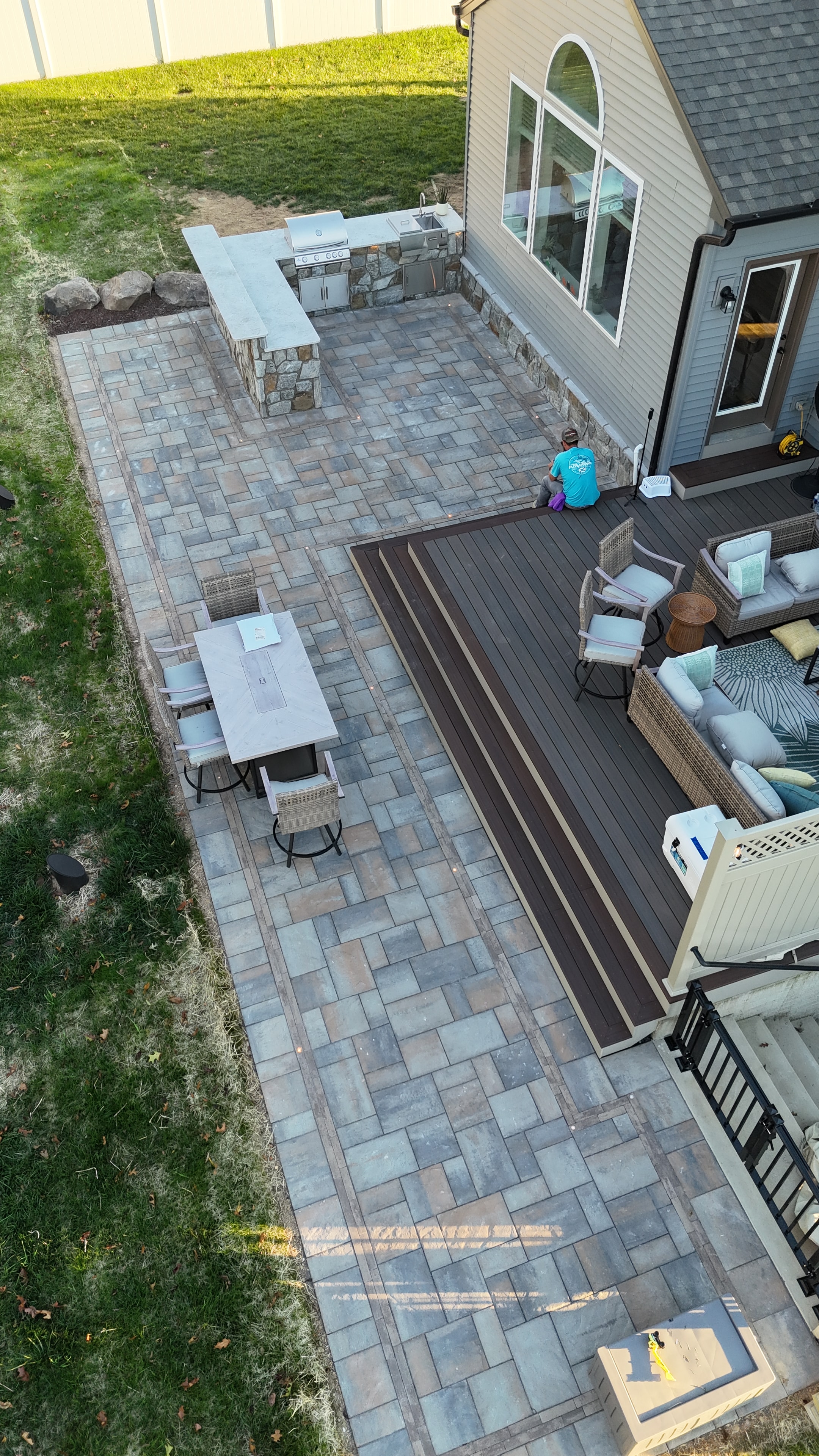 Chef's Dream — aerial overhead shot of paver patio with LED dot lights, composite deck, and outdoor kitchen with granite countertop and stone surround
