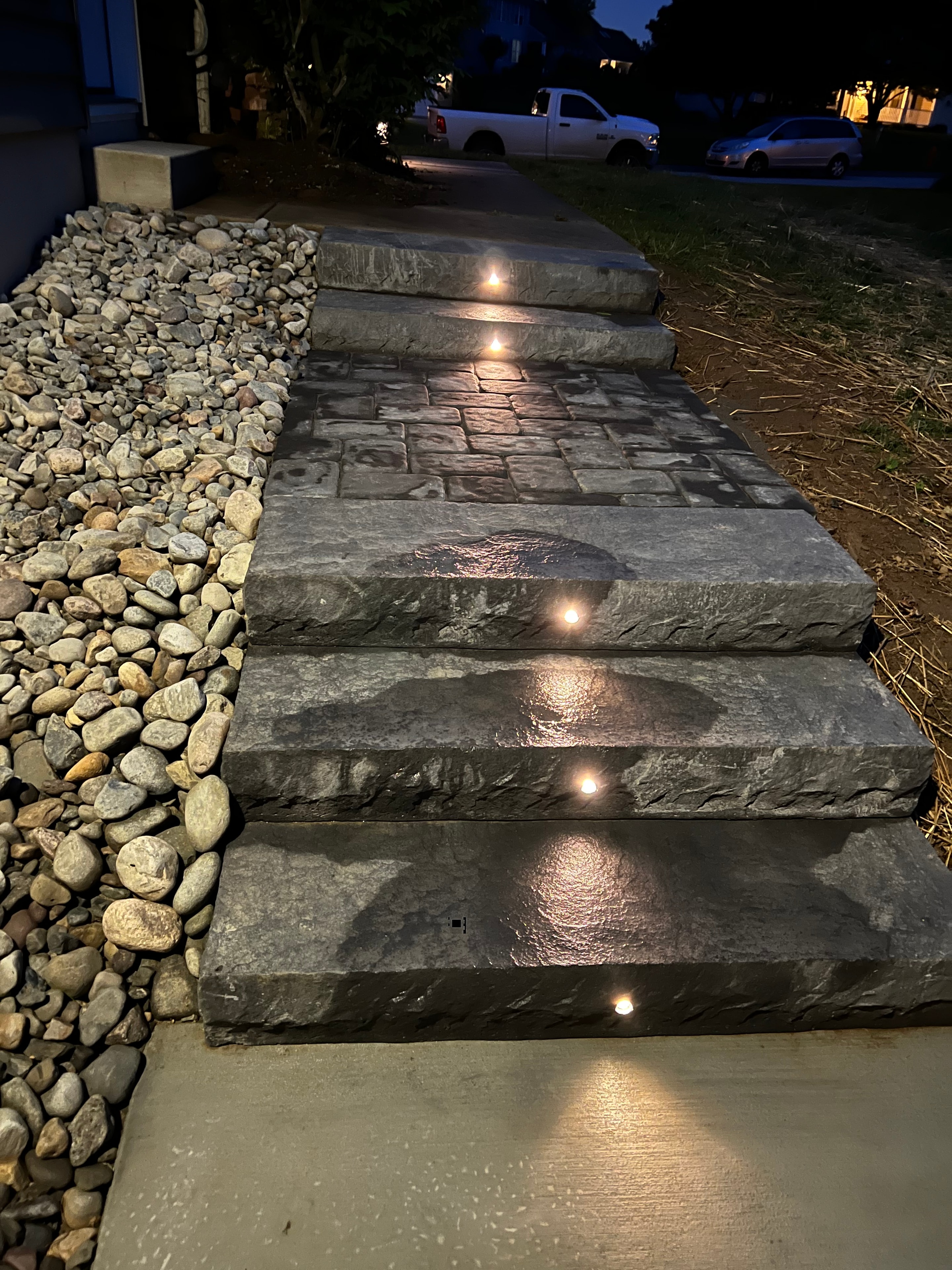 Concrete Jungle — nighttime close-up of LED-lit natural stone retaining wall with river rock base and warm uplighting