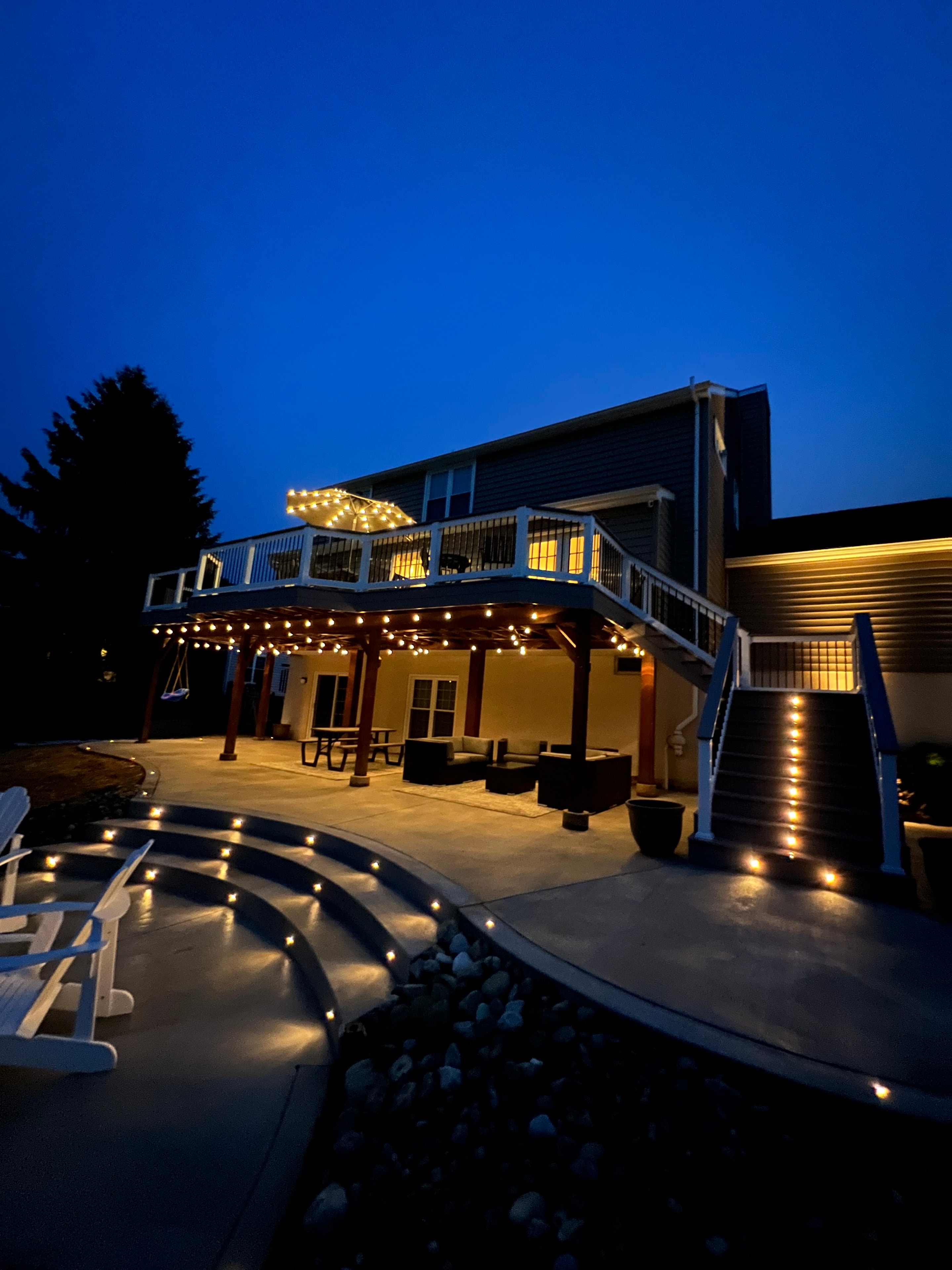 Concrete Jungle — dusk close-up of multi-level deck staircase with LED step lights, string lights, and circular concrete patio edge