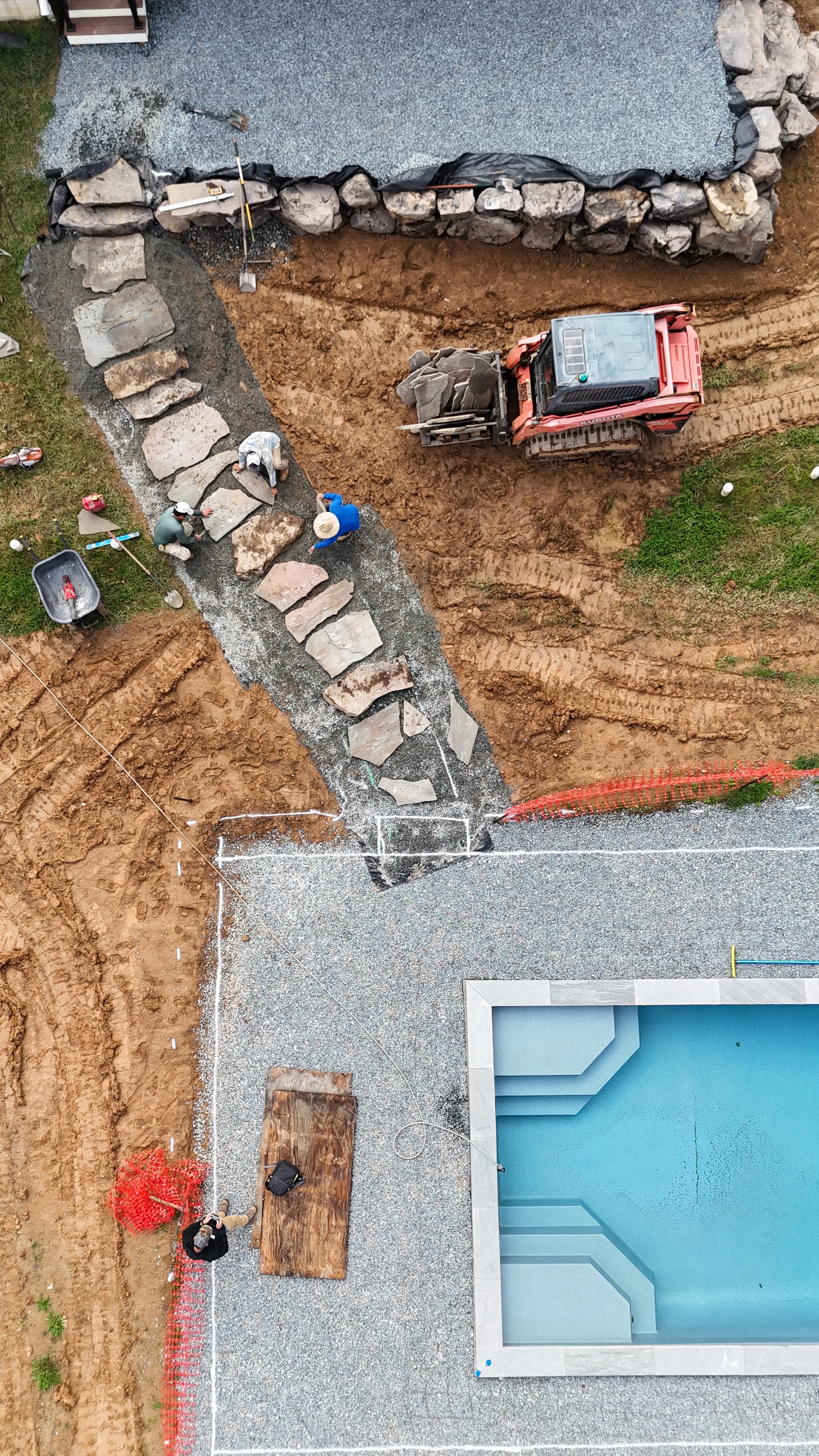 Under construction — aerial view of crew laying stone pathway beside pool