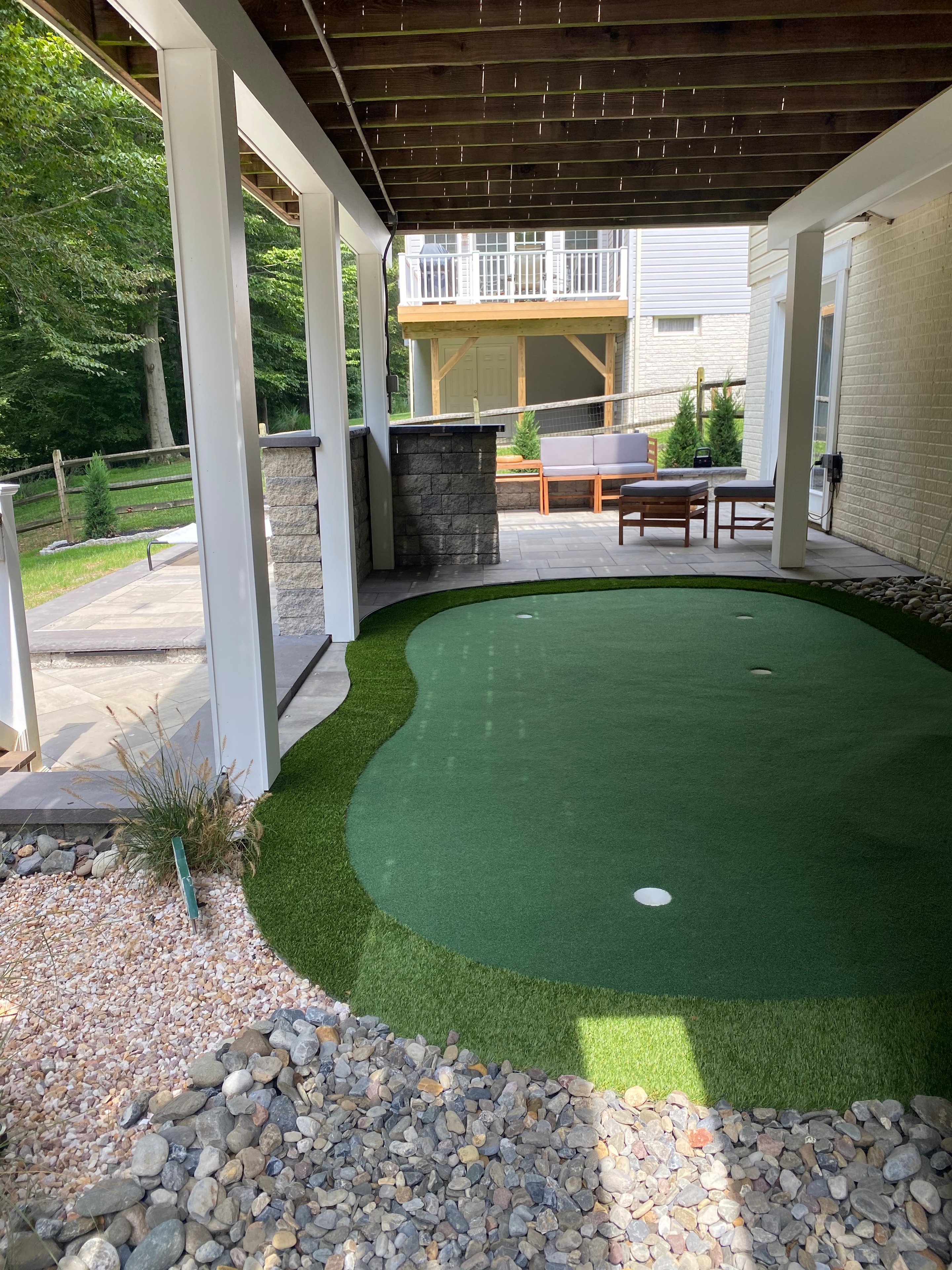 Golfing Paradise — daytime view of putting green with river rock border, paver patio, and pergola posts