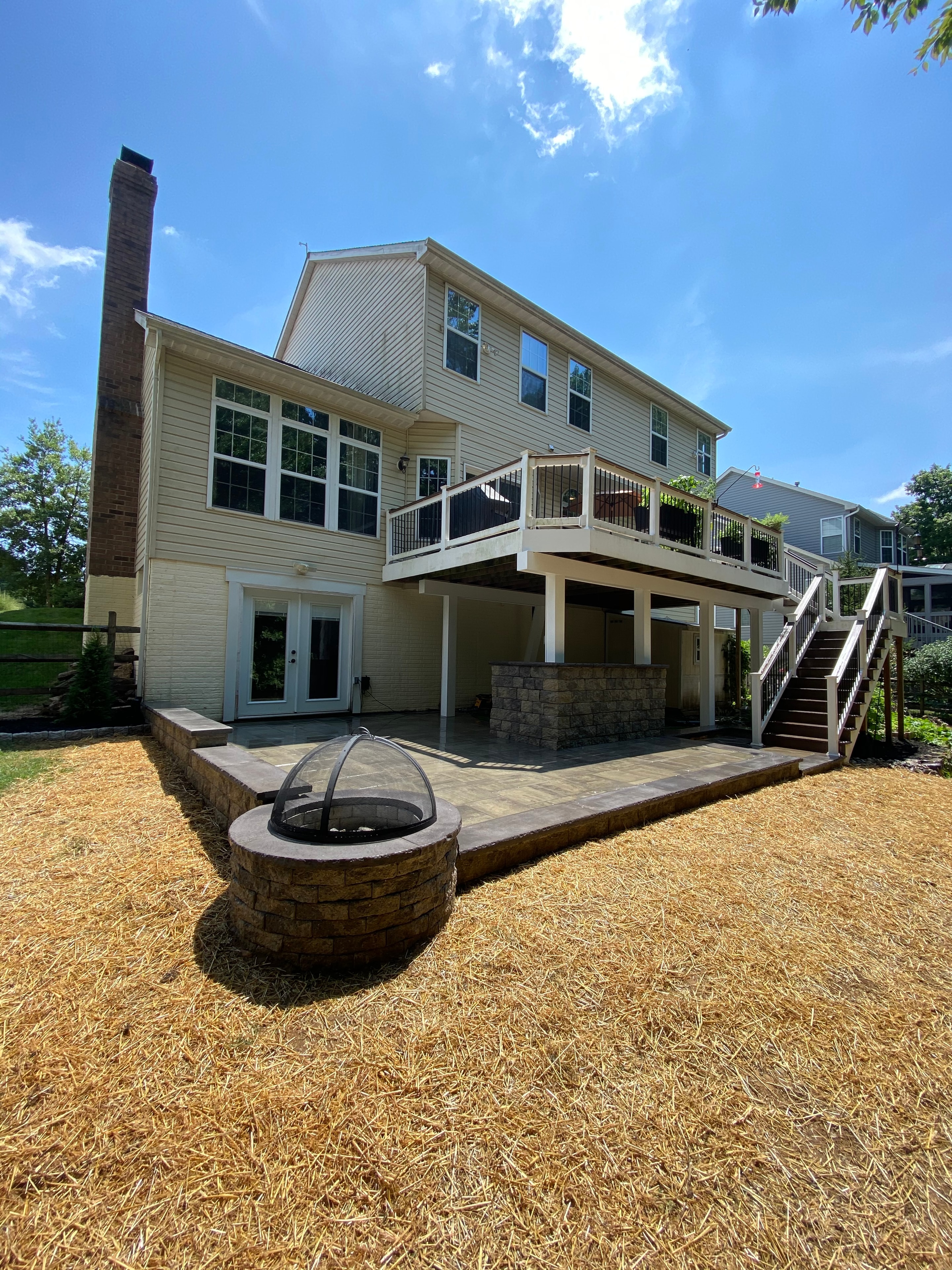 Golfing Paradise — wide daytime shot of full backyard with multi-level deck, paver patio, fire pit, and straw-covered lawn