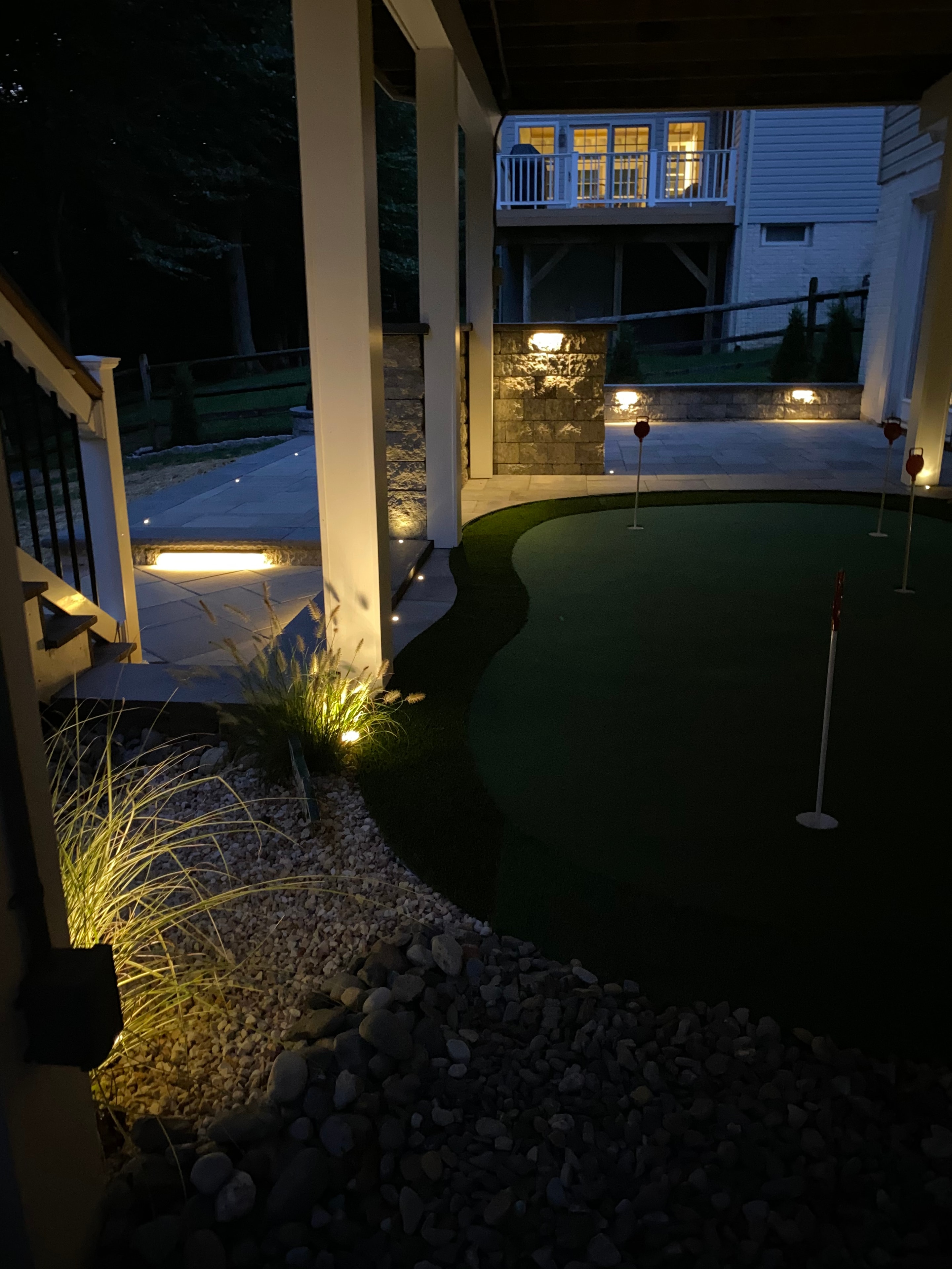Golfing Paradise — nighttime shot of putting green with LED-lit pergola, warm landscape lighting, and river rock border