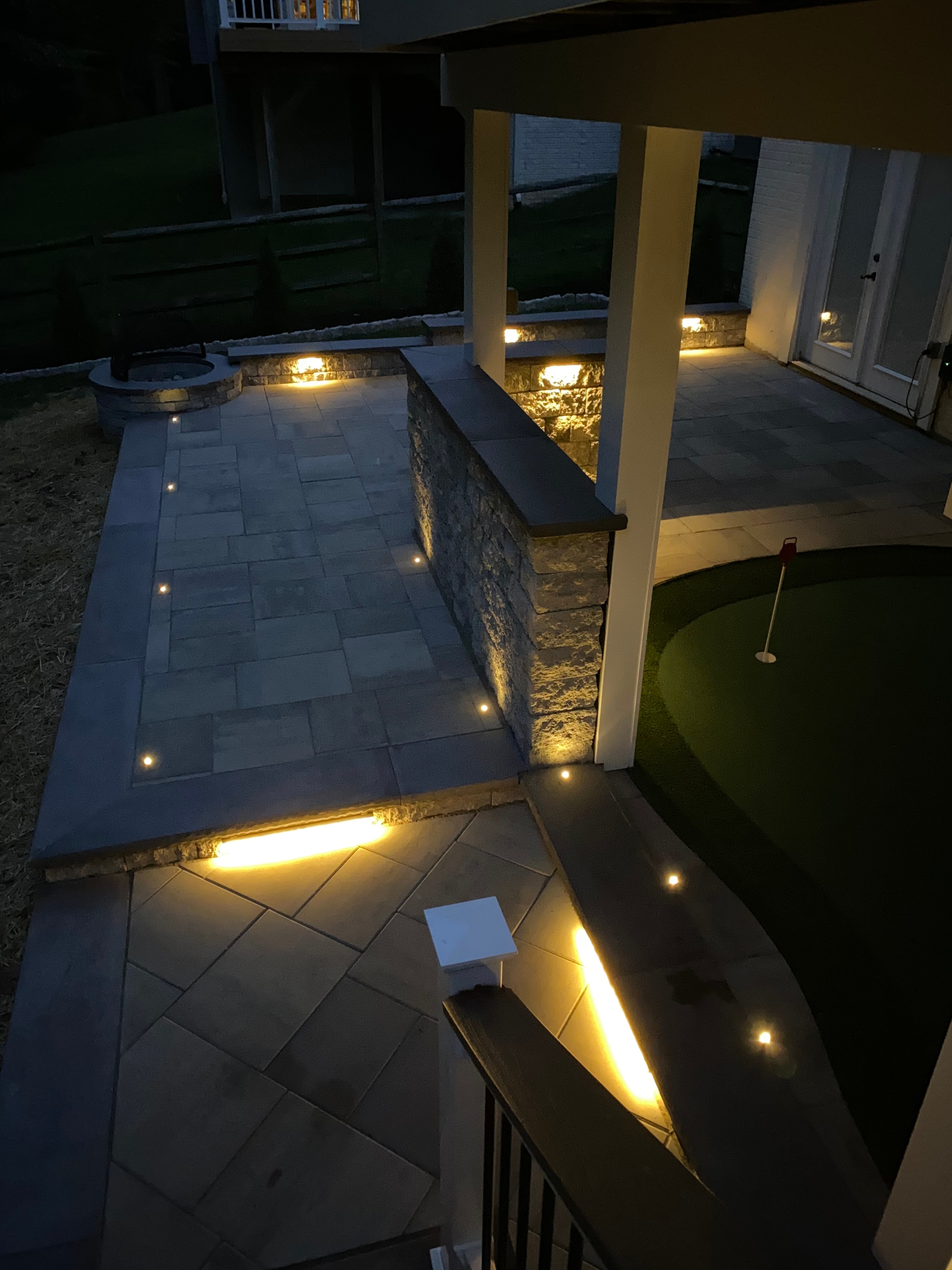 Golfing Paradise — nighttime close-up of paver patio with LED step lights, granite sitting wall uplighting, and putting green