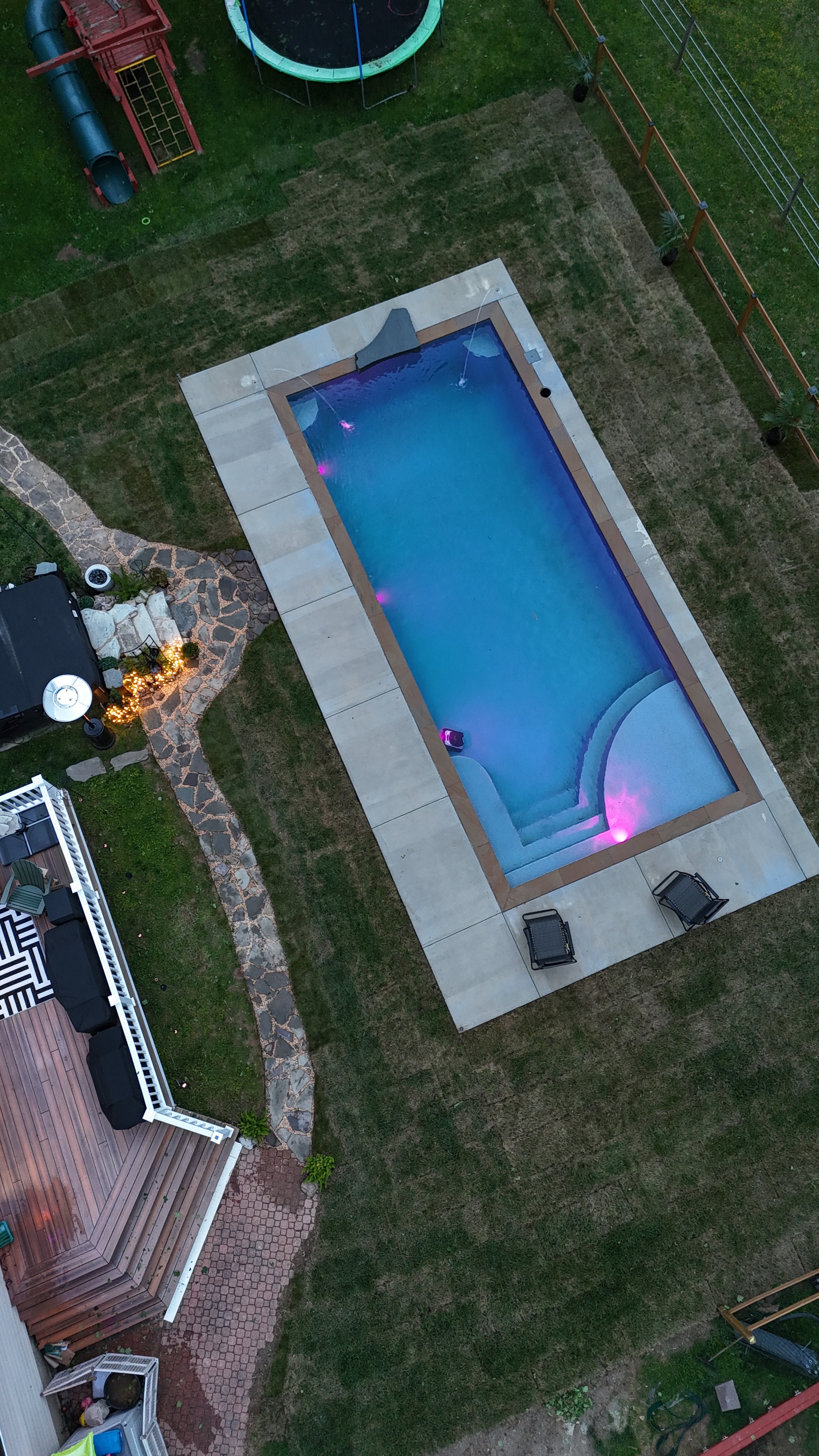 Light Up the Night — angled aerial of pool glowing purple with deck and stone path lit up