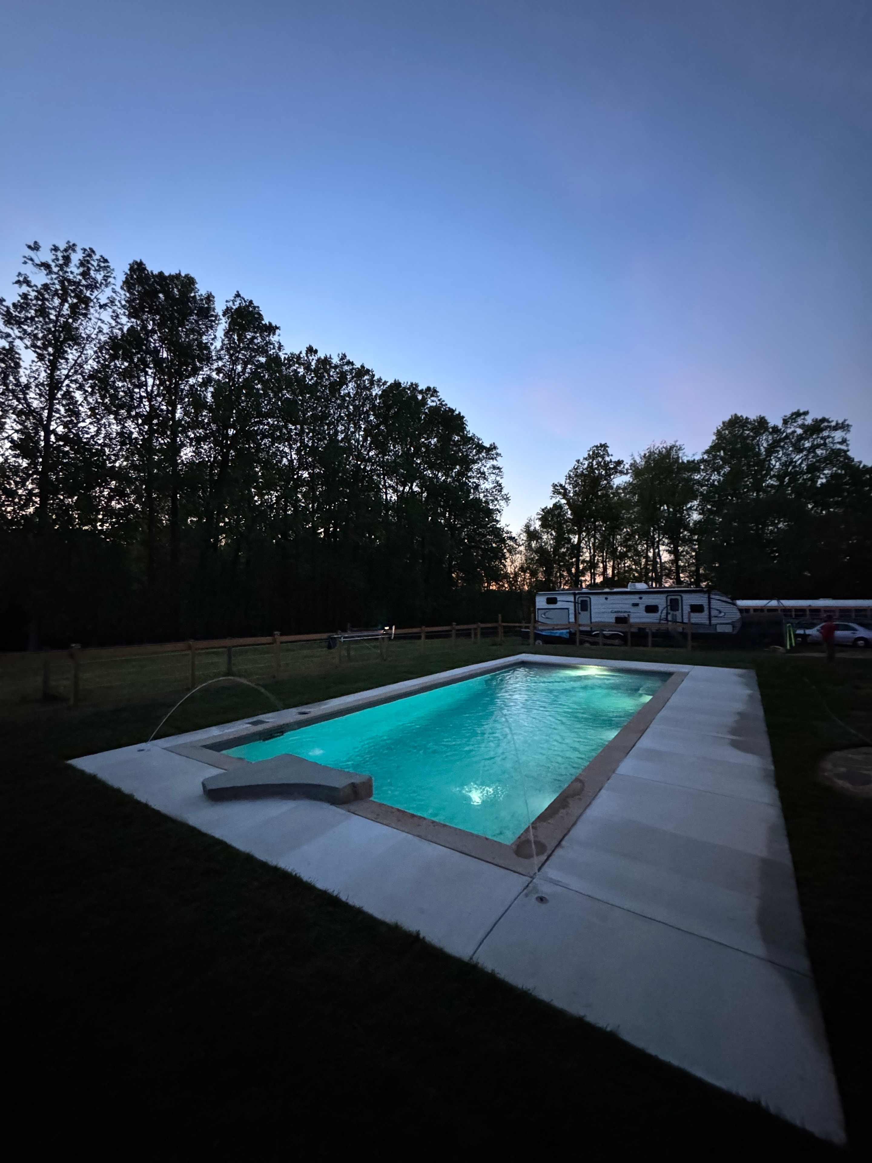 Light Up the Night — ground-level dusk shot of pool glowing teal with treeline silhouette