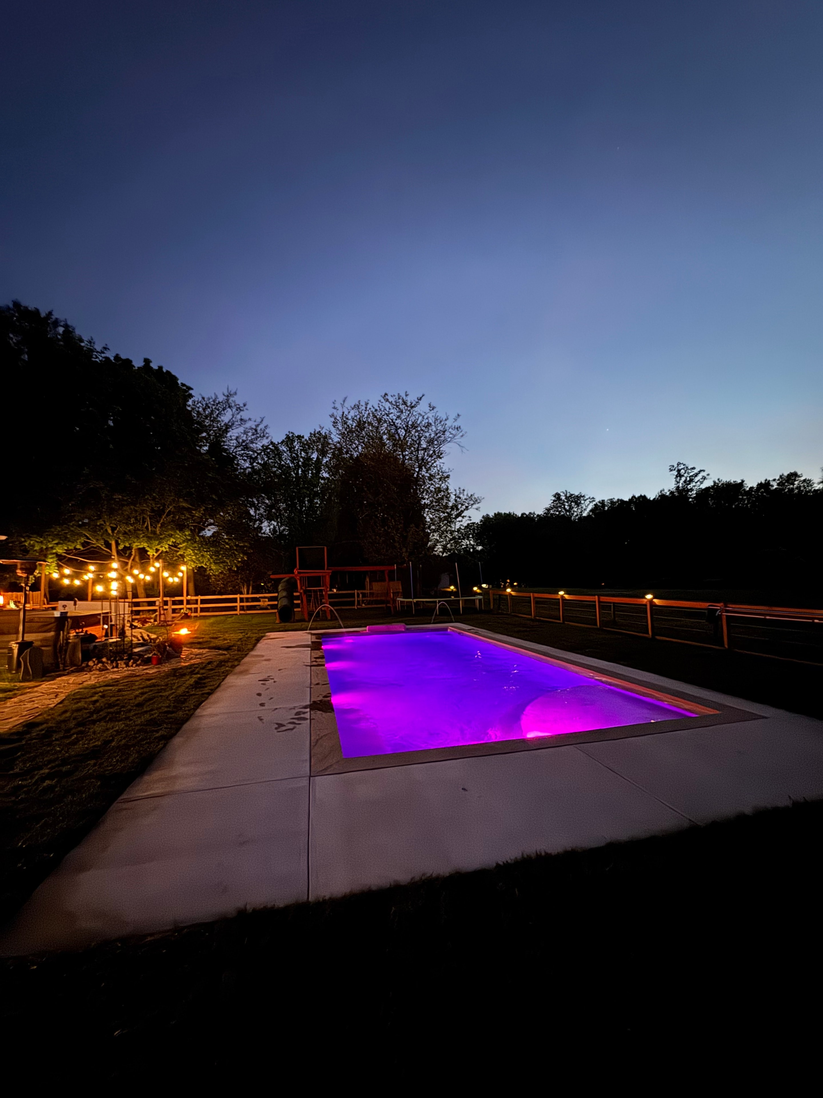 Light Up the Night — ground-level night shot of pool glowing purple with string lights along fence