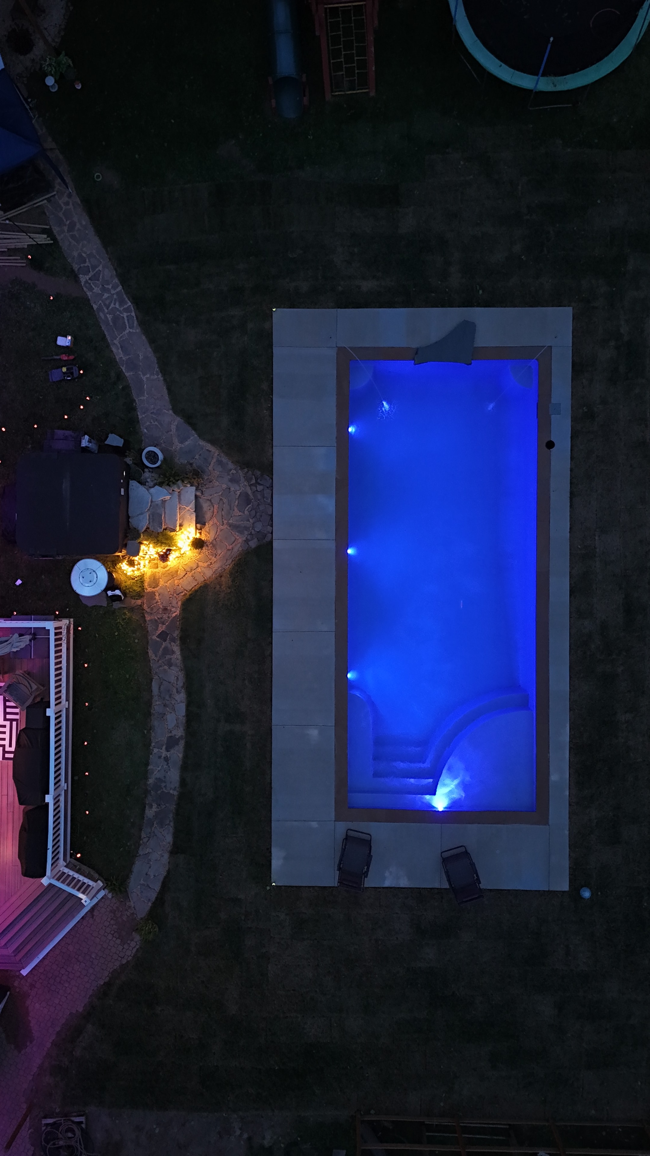 Light Up the Night — aerial night shot of pool glowing blue with stone path and fire pit lit up