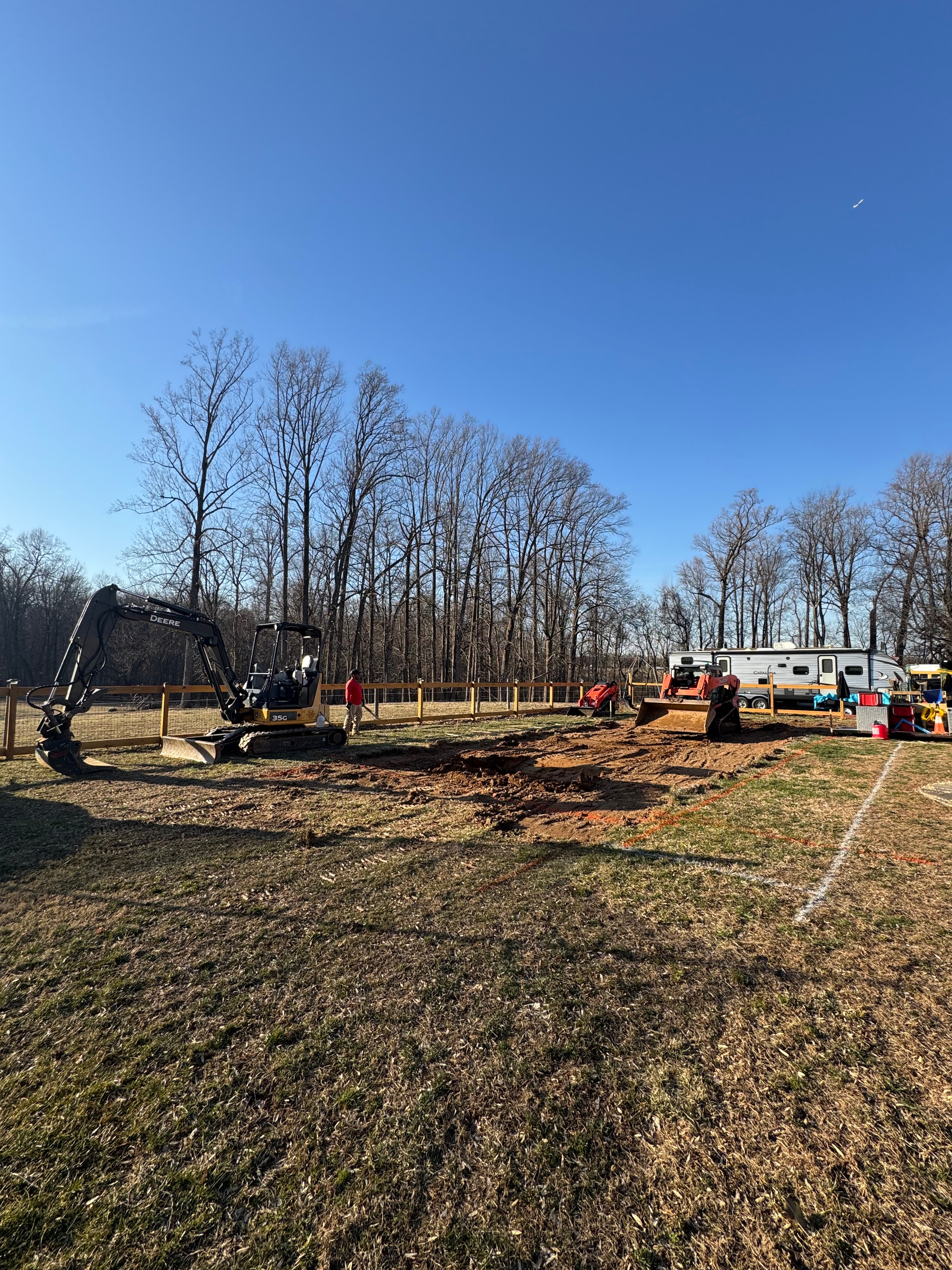 Under construction — John Deere excavator and equipment lined up along cleared site perimeter