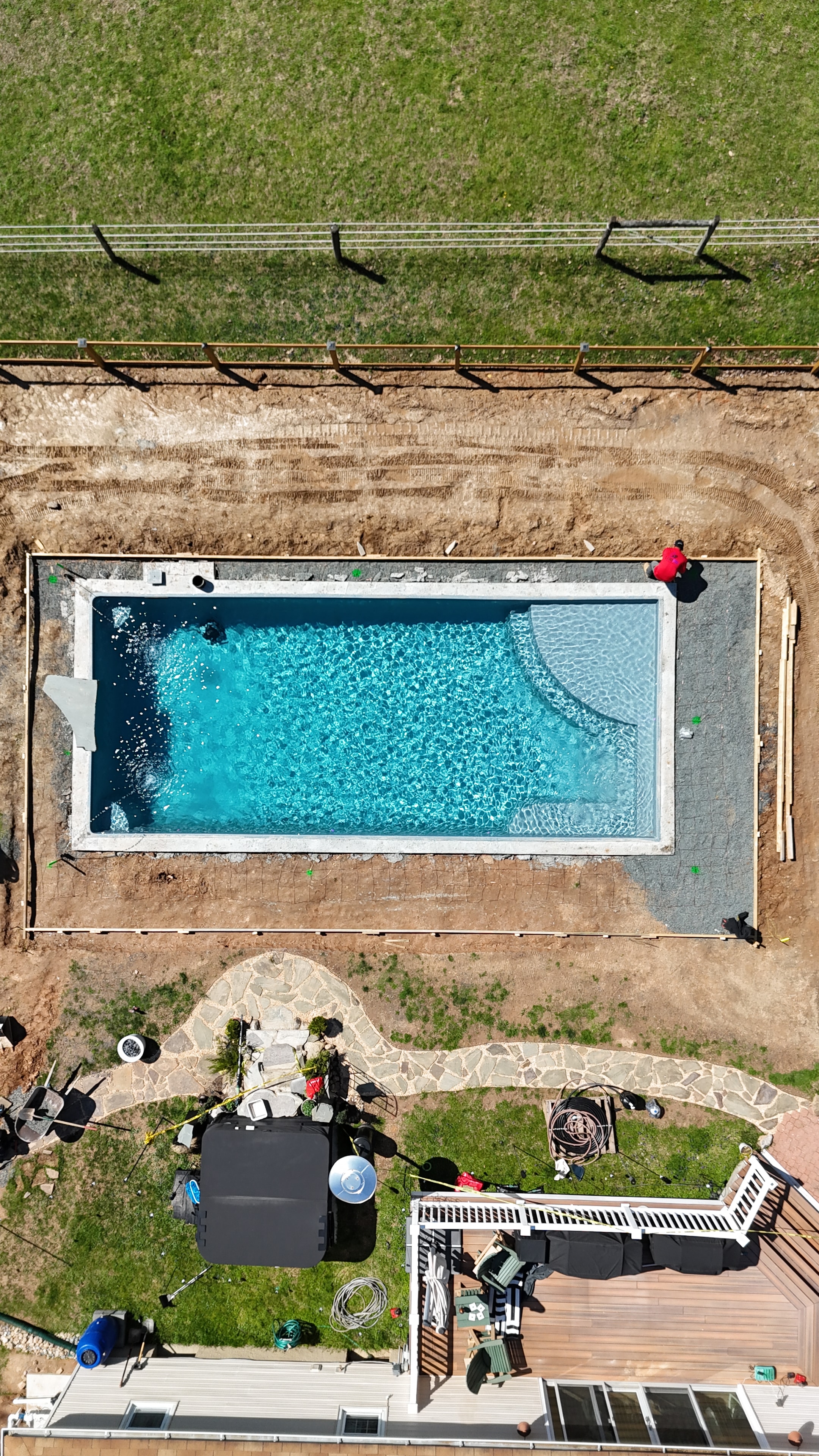Under construction — aerial view of pool shell filled with water, stone pathway and deck framing visible beside house