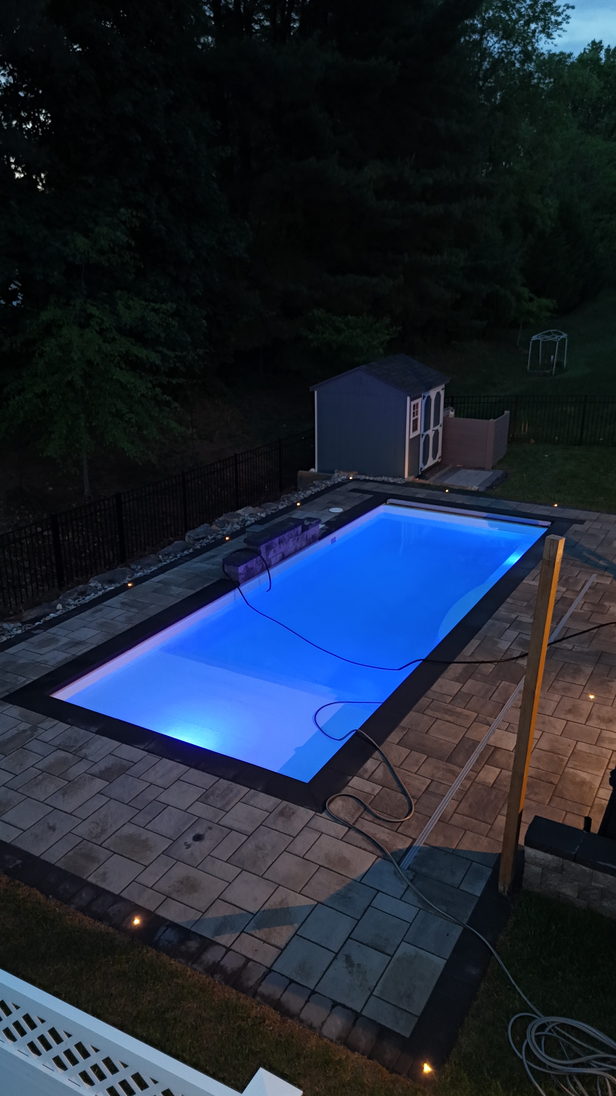 Small but Mighty — close-up dusk shot of pool glowing blue with paver coping detail