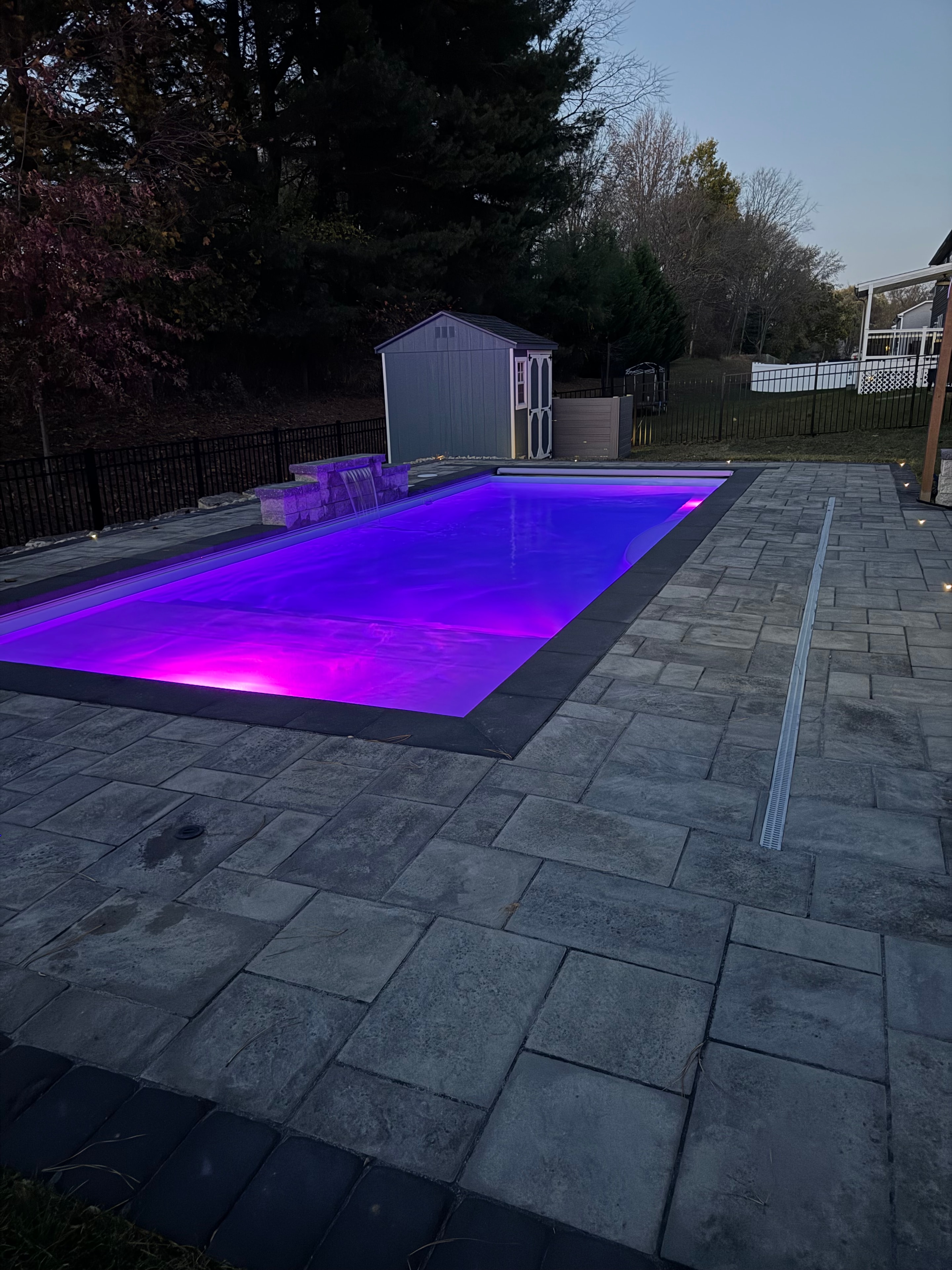 Small but Mighty — dusk aerial of pool glowing purple with paver surround and pathway lights
