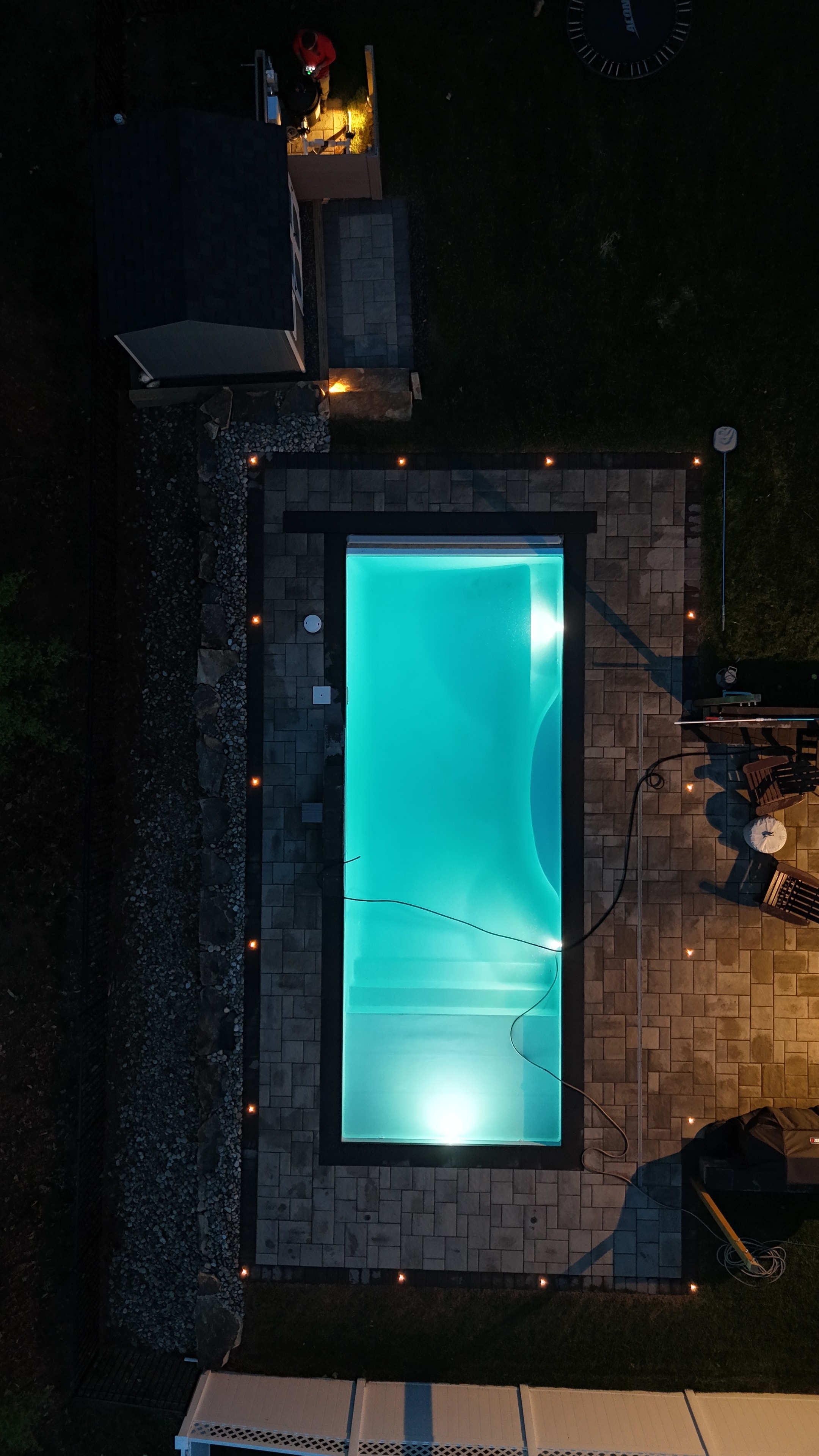 Small but Mighty — aerial night shot of pool glowing teal with paver surround and pathway lights