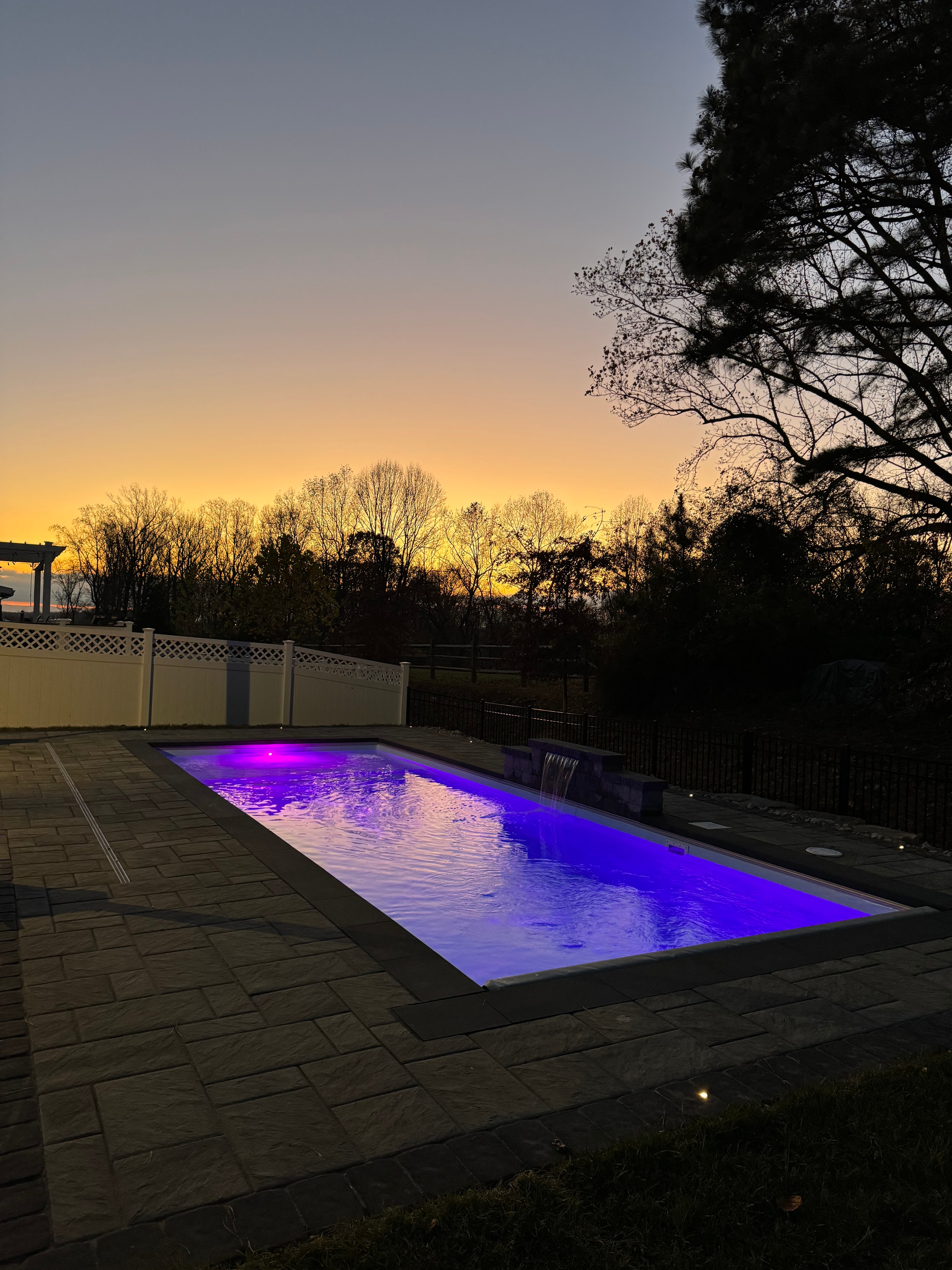 Small but Mighty — dusk shot of pool glowing purple with waterfall and sunset sky silhouette