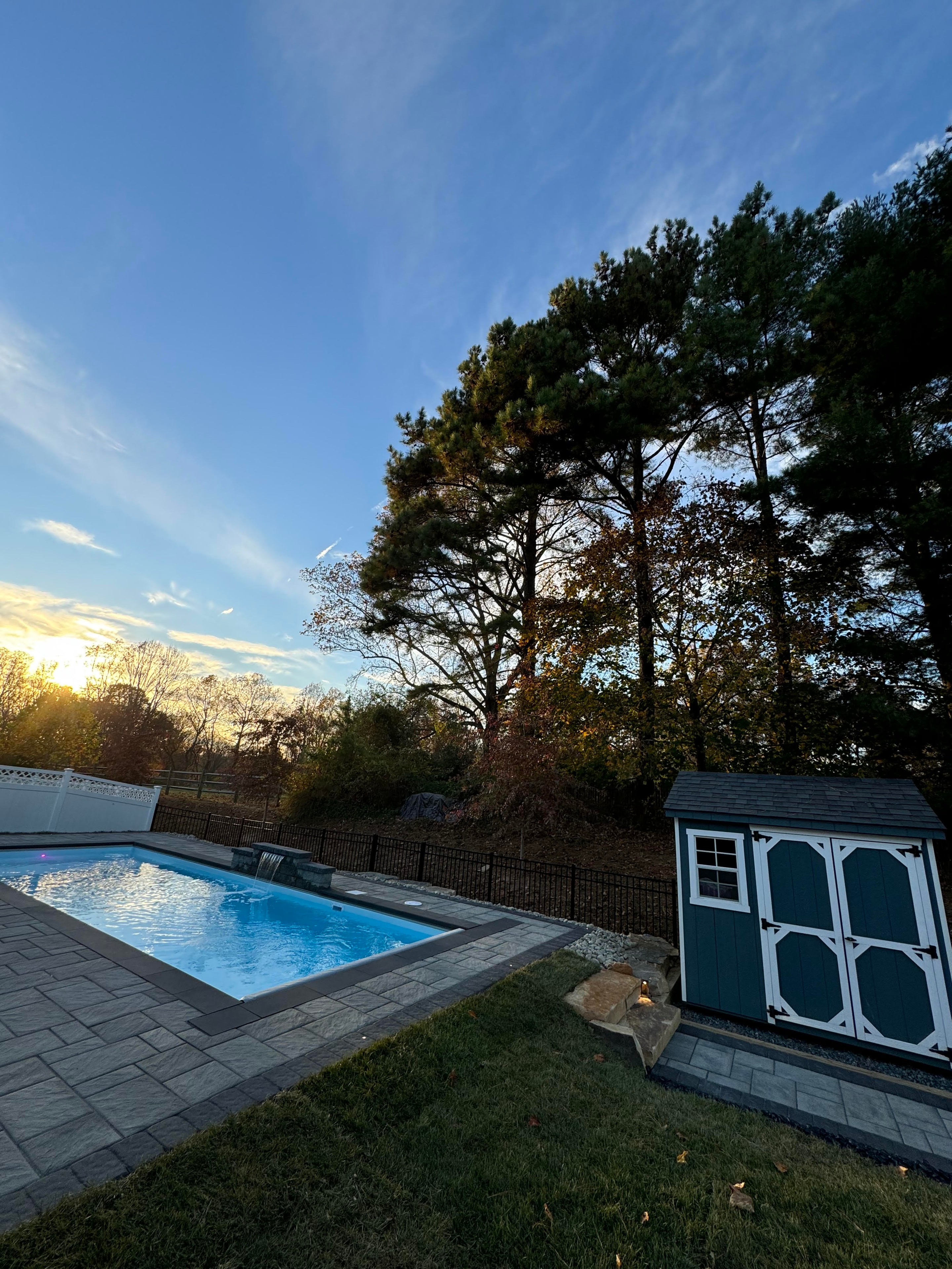 Small but Mighty — sunset view of pool with paver patio, shed, and treeline in background