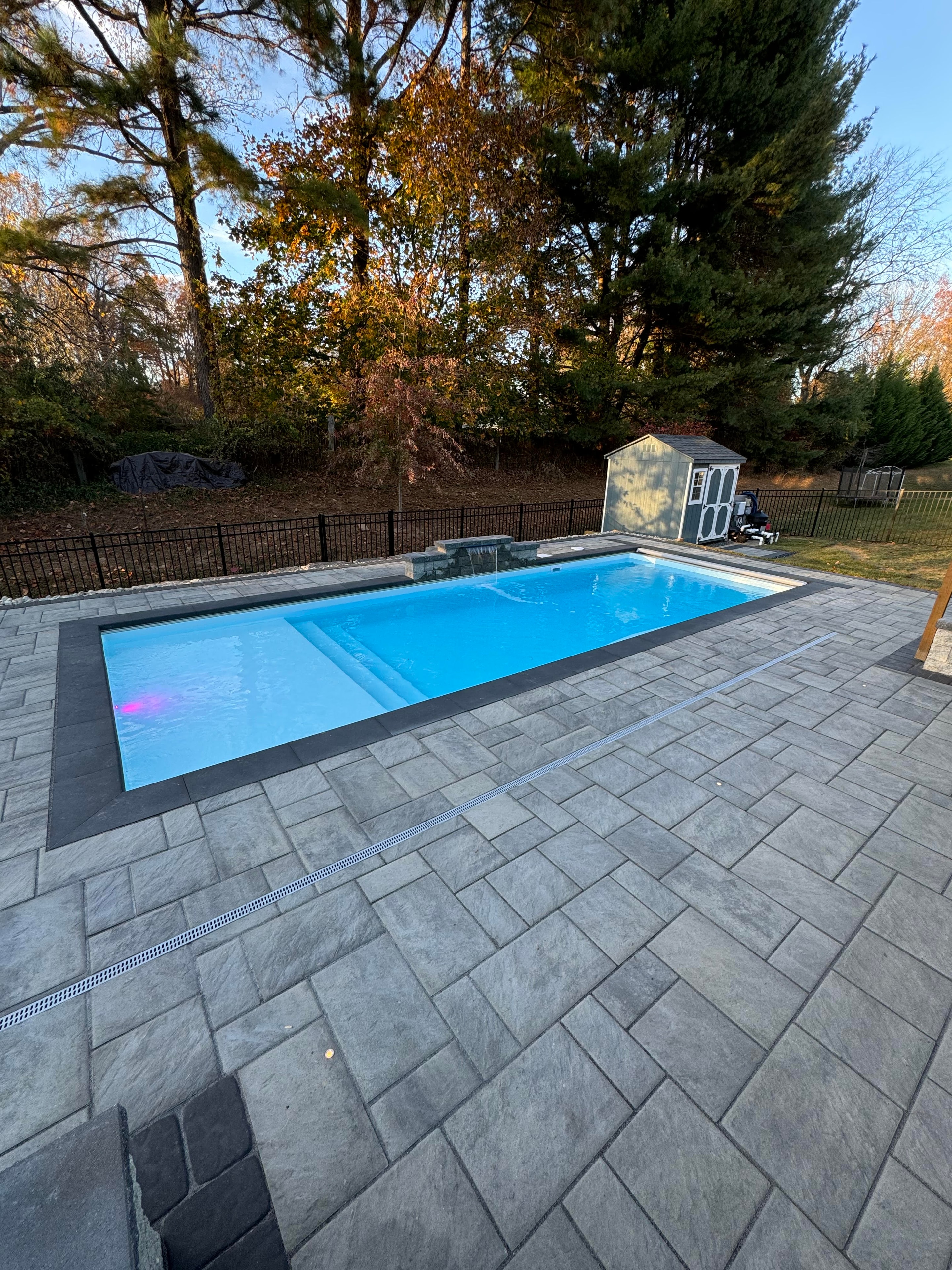 Small but Mighty — daytime close-up of pool with paver coping, waterfall, and shed in background
