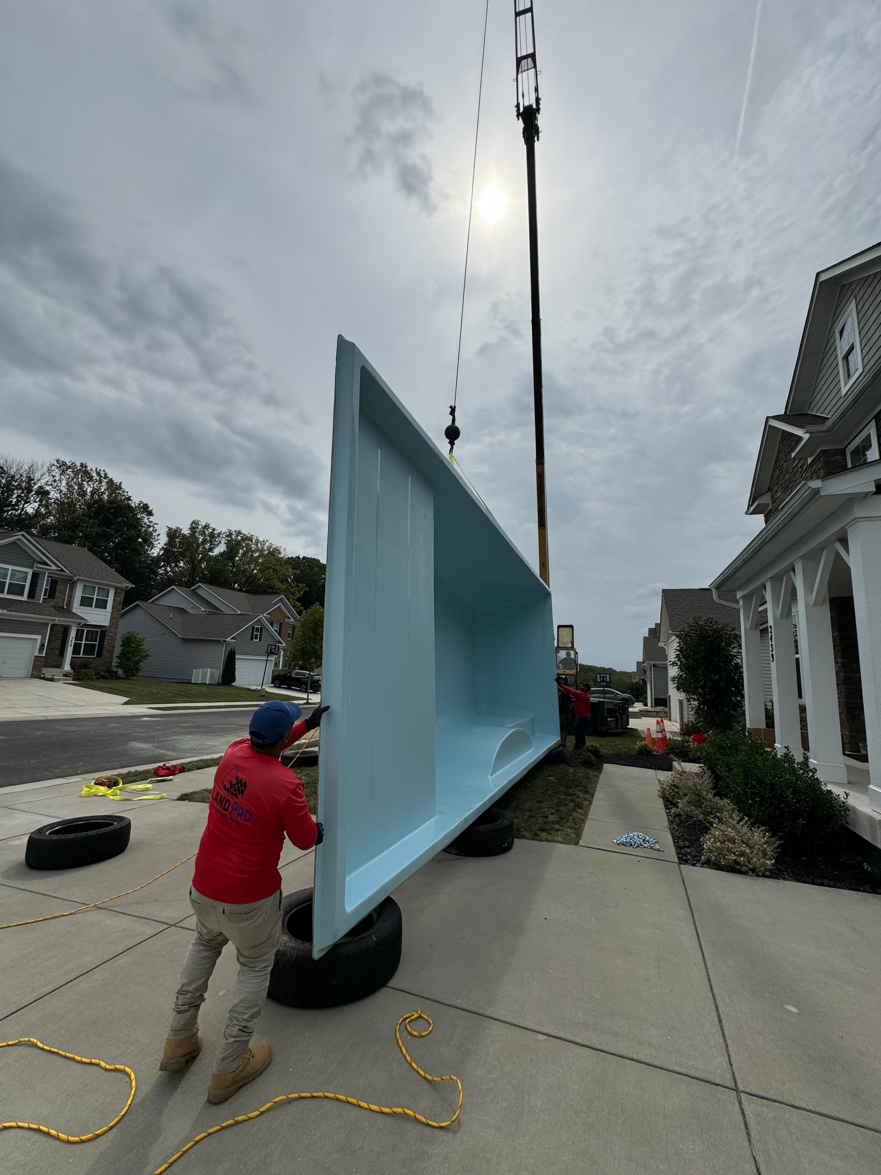 Under construction — fiberglass pool shell being crane-lifted into position on the street in front of house