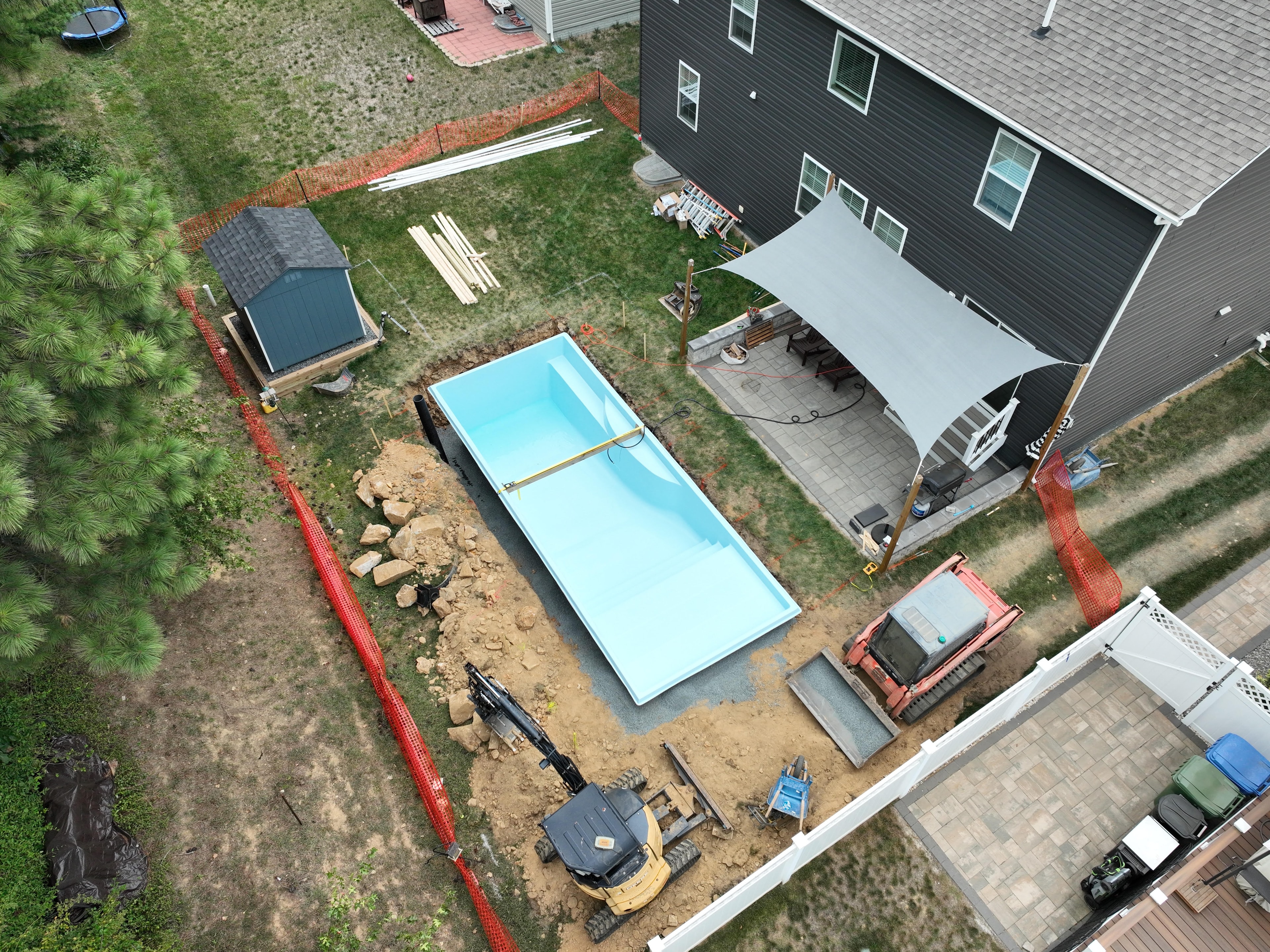 Under construction — aerial view of pool shell installed in backyard with excavators still on site and shade sail visible