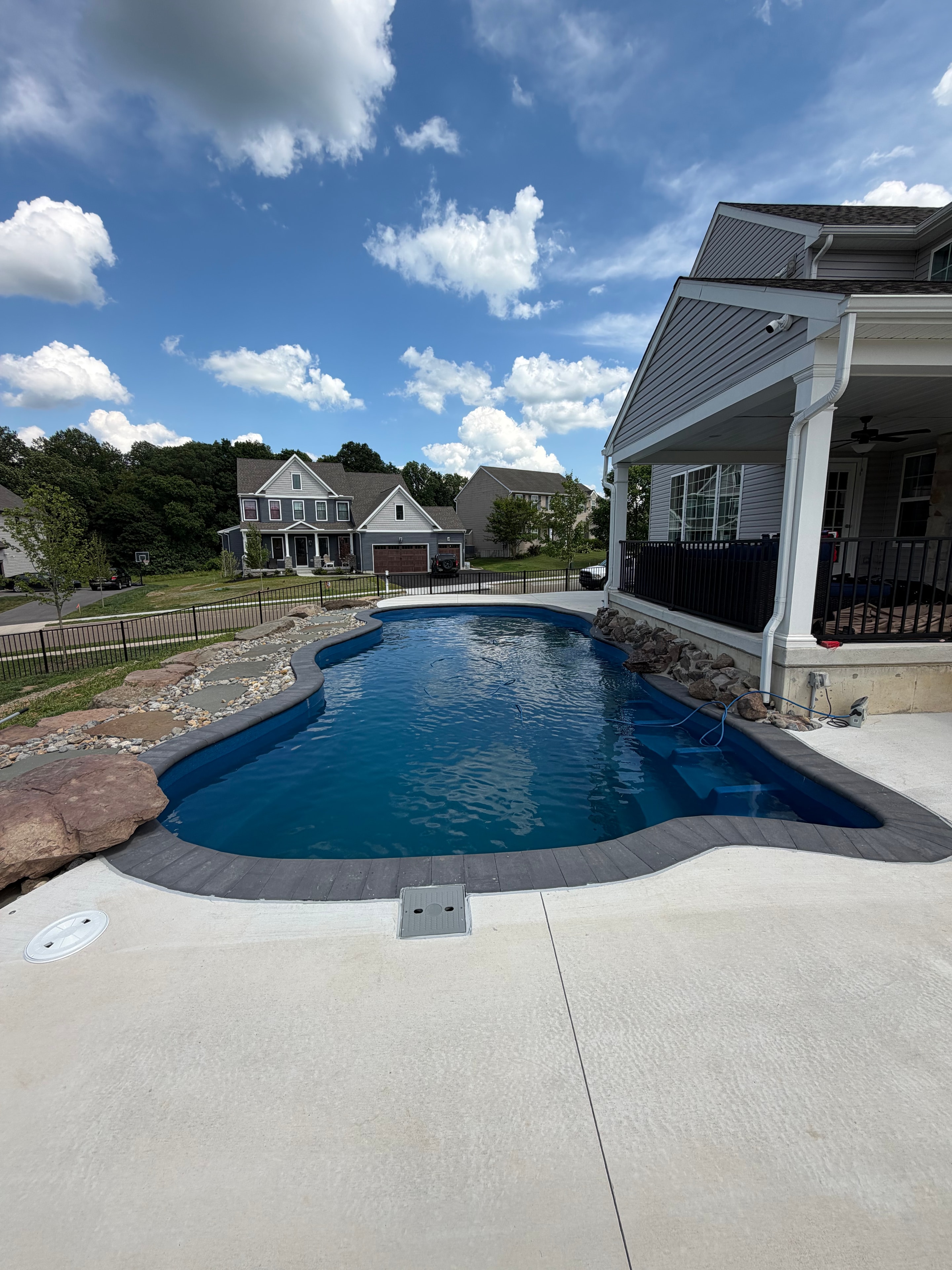 Tight Quarters — daytime view of fiberglass pool with concrete patio, rock landscaping, and pergola under blue sky